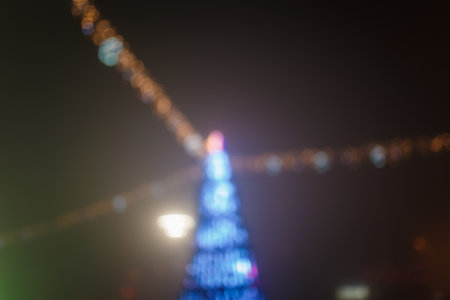Unfocused night shot of Christmas tree with garland lights bokeh in the city. Happy New Year, Merry Christmas, winter holidays concept.の写真素材