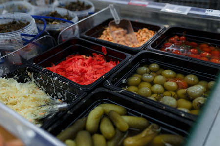 Soft focused shot of vegetable department in grocery store, supermarket, mall, hypermarket or shopping center. Boxes with pickled green and red tomatoes, cabbage, ginger, shrimps and cucumbers.の写真素材