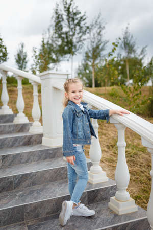 Little smiling girl posing in jeans jacket on stairs outdoorsの写真素材