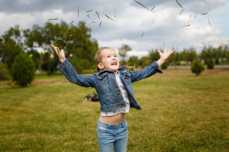 Little girl jumping and throwing green grass on lawn in spring park. Happy joyfull emotion, carefree childhood, outdoors activityの写真素材