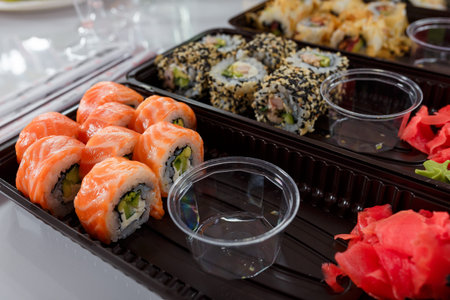 Sushi set, salmon rolls, pickled ginger, wasabi in disposable container, empty pots for soy sauce....