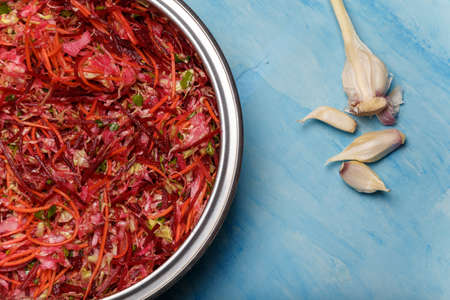Metallic bowl of salad called Brush. Beetroot, carrots and cabbage cut into thin strips with garlic on blue wooden background. Vegetarian, organic, healthy food, diet, nutrition. Top view, copy space.の写真素材