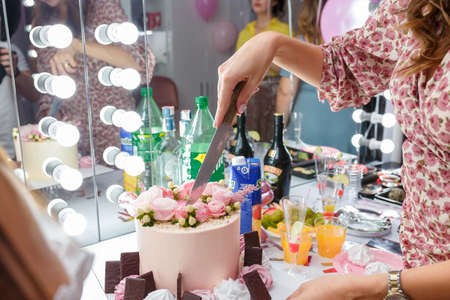 Izmail, Ukraine, August 2020. Female hands with knife cut beautiful pink cake with rose flowers. Festive candy bar for birthday party, anniversary or women holiday.のeditorial素材