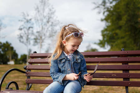 Little girl sitting on bench in spring park. Outdoors walk and child activity.の写真素材