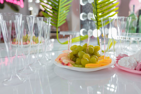 Soft focused close up shot of fruit cut platter, orange, apple and grapes, sweet pink white zephyr or marshmallow. Unfocused coctail glassess on background. Wedding, birthday party, festive event candy bar.の写真素材