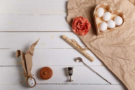 Izmail, Ukraine. April 2020. Heart shaped box with boiled eggs, salt pot, fabric rose flower and Easter bunny made from egg and paper ears on wooden white background. Easter and spring concept. Top view, copy space.のeditorial素材