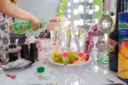 Izmail, Ukraine, August 2020. Festive table, martini coctail glasses, berries and lime slices, fruit cut platter, drinks. Blurry cake, sweet zephyr, female hands on background.のeditorial素材