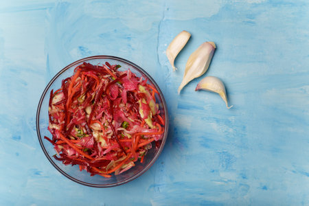 Bowl of salad called Brush. Beetroot, carrots and cabbage cut into thin strips with garlic on blue wooden background. Vegetarian, organic, healthy food, diet, nutrition. Top view, copy space.の写真素材