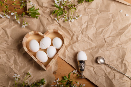 Heart shaped wooden box with boiled Easter eggs, one egg in egg cup with silver spoon and cherry...