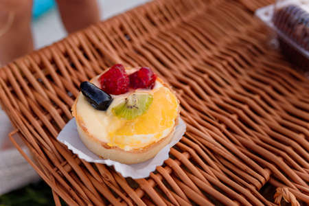 Soft focused shot of sponge cake with fruits on wicker basket background. Outdoor picnic, sweet pastry.の写真素材