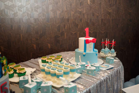 Izmail, Ukraine - May 2020. Festive candy bar for one year old boy birthday party. Cake with red number 1 and butterfly bow on shirt. Blue cakepops, cupcakes with red bows and Teenage Mutant Ninja Turtles.のeditorial素材