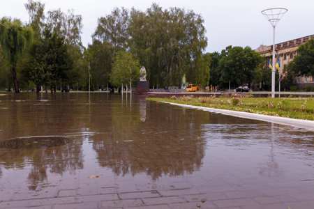 Soft focused shot of town streets flooded by heavy rain. Thunderstorm consequences. Big puddle with tree reflection on asphalt tile. Climate changes, adverse weather conditions, ecological problem.の写真素材