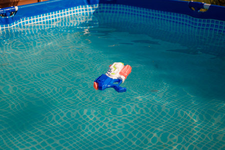Water pistol swimming in pool, blue transparent water in sun rays. Outdoors summer activities for children.の写真素材