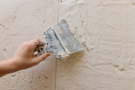 Male hands with spatula using putty for wall, builder making overhaul.の写真素材