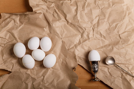 Boiled eggs and egg in silver egg cup with spoon on paper background. Lunch or Easter concept. Top view, copy space.の写真素材