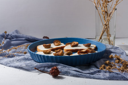 Bread with cheese and figs on blue plate, vase of dry flowers on background. Healthy breakfast,...