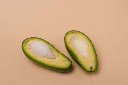 Two halves of green fresh avocado with seed on beige background. Minimal styled composition.