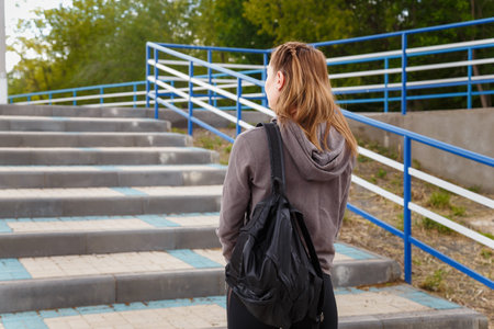 Young woman back to camera in sportswear with backpack going to stadium to make physical exercises.