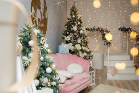 Izmail, Ukraine. December 2020. Room decorated for Christmas and New Year celebration. Pink sofa with cushions, fir-trees and white stairs. Holiday spirit. Modern interior.のeditorial素材