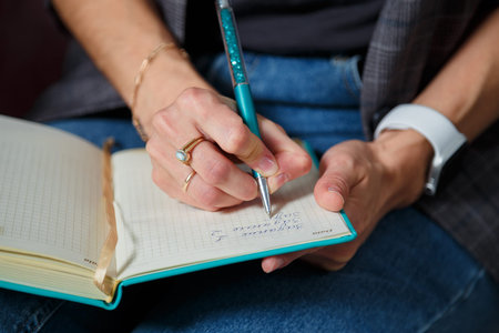 Soft focused close up shot of woman in jeans, gray jacket sitting with notebook, only hands writing...