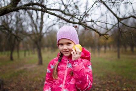 Little girl in pink jacket holding apple in autumn forest
