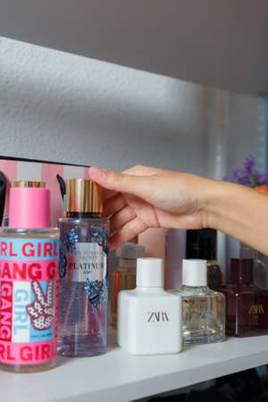 Izmail, Ukraine. May 2021. Female hands putting parfume bottle on shelf with other bottles and cosmetics. Beauty concept. Vertical close up shotのeditorial素材