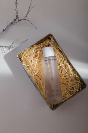 Izmail, Ukraine, July 2021. Bottle of essence toner in box with wood shavings filler in trendy natural solid light. Face skin care cosmetics, copy spaceのeditorial素材