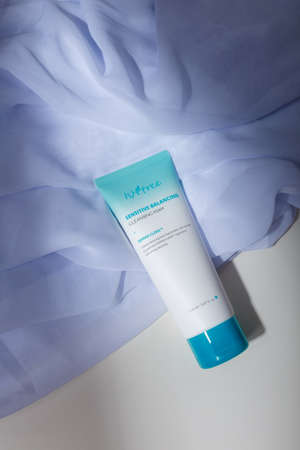 Izmail, Ukraine, July 2021. White tube with blue cap on white fabric, with natural solid shadows. Face skin care cosmetics, cremeのeditorial素材