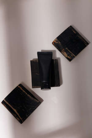 Black tube of clay mask, creme, scrub for face, skin care cosmetics on wooden board mat in solid light with shadow play on whiteの写真素材