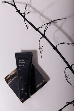 Izmail, Ukraine, July 2021. Black tube of clay mask for face, skin care cosmetics with branch on board in solid light with shadow play on whiteのeditorial素材