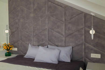 Beautiful gray bedroom, bed, pillows, soft fabric headboard, autumn bouquet of yellow chrysanthemums in green vase near. Modern interior designの写真素材