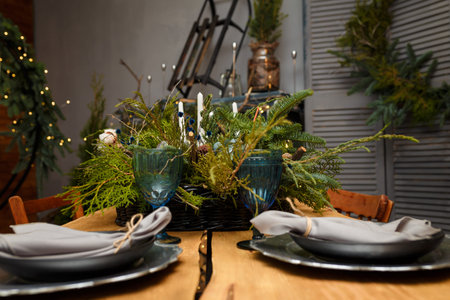 Rustic style Christmas festive table, blue glasses, plates and fresh thuja, fir branches bouquet...