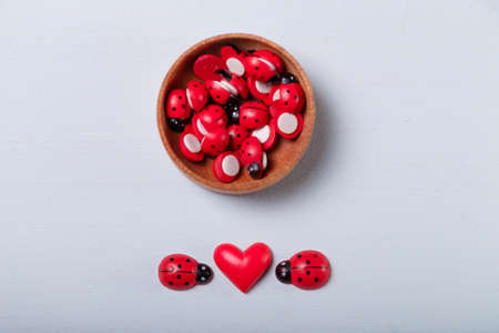 Wooden bowl with small wooden decorative red ladybugs for handwork, handmade decorations, leisure time with children. Spring and love, first date, Valentines day concept. Copy space.の写真素材