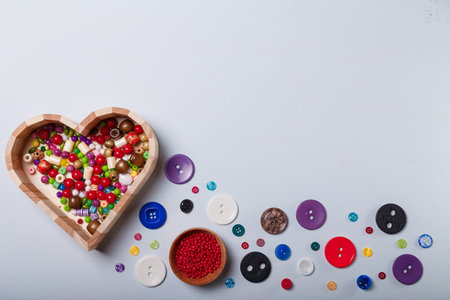 Close up of wooden heart shaped box of multicolored beads and buttons for sewing and embroidery. Set...