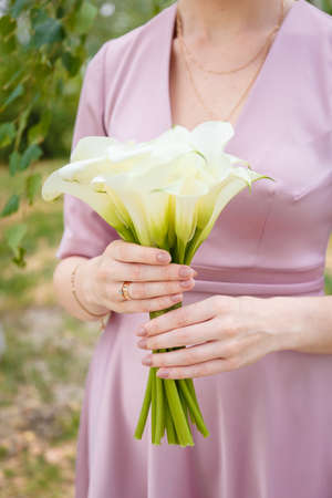 Bride in tender pink wedding dress holding white calla lilies bouquet. Minimalists style dressing, nude manicure. Closeup vertical shot.の写真素材