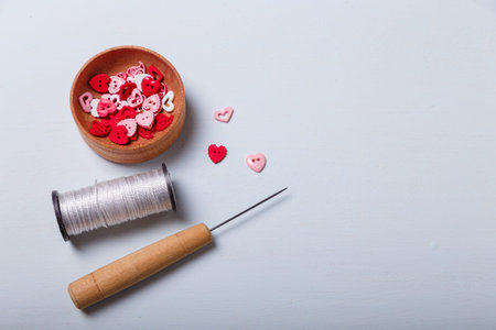 Wooden bowl of heart shaped red and pink buttons with spool of threads and awl for sewing and...