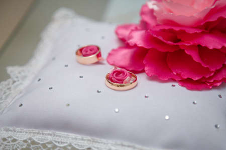 Two golden wedding rings on white decorative cushion with pink peon flower. Spring wedding details.の写真素材