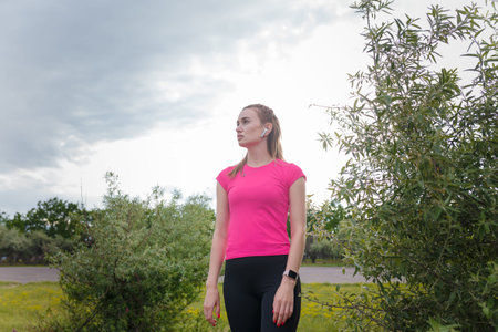 Portrait of young woman in sportswear and wireless earphones getting ready for outdoors running or...