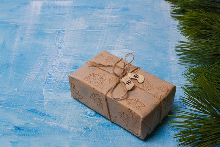 No plastic Merry Christmas present wrapping. Gift box in kraft paper, jute rope bow on blue painted background, pine branches frame. Copy spaceの写真素材