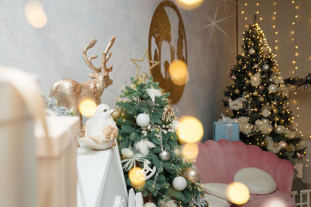 Izmail, Ukraine. December 2020. Christmas, New Year celebration. Pink sofa, 2 fir-trees, piano, wooden picture with reindeers. Holiday spirit, waiting for miracle. Modern decorated room interior.のeditorial素材