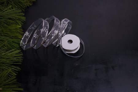 Silver ribbon tape on black painted background, pine branches frame. Minimalists Christmas present...