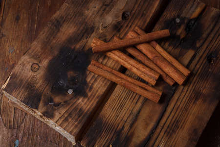 Cinnamon aromatic sticks on kitchen board, wooden table. Spices, flavors for pastry, hot autumn and winter savory drinksの写真素材
