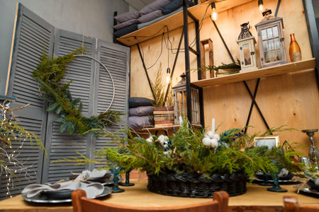 Izmail, Ukraine. December 2020. Soft focused shot of rustic style Christmas festive table, fresh thuja branches bouquet. Eco-friendly green decorative elements. Books and lanterns on wooden background.のeditorial素材