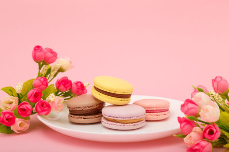 Plate of macaroons on pink background with flowers. Sweet pastry, baked products, sweets, dessert. Unhealthy diet, sugar dependence.の写真素材