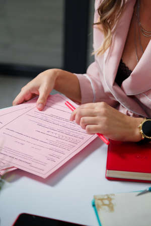 Izmail, Ukraine. May 2021. Business woman in pink jacket writing in notebook. Only hands, pen, glasses, smartphone on table visible. Vertical closeup shotのeditorial素材