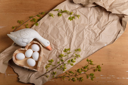 Wooden heart shaped box with Easter eggs, goose toy and branch with fresh green foliage on paper background. Easter and spring concept. Top view, copy space.の写真素材