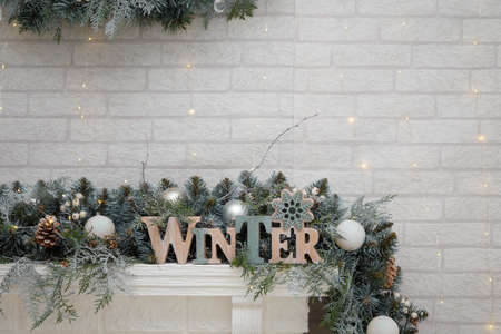 Word Winter from wooden letters among fir branches with white baubles, cones, snowflakes on top of fireplace, brick wall backgroundの写真素材