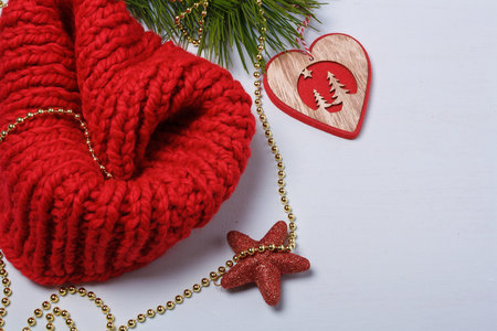 Red knit snood, pine branch, red star, wooden heart shaped toy with golden beads on light background. Christmas card, copy spaceの写真素材
