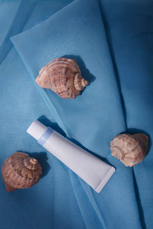 White mockup tube no label on blue fabric, with natural sea shells. Template, copy space. Face skin care cosmetics, cremeの写真素材