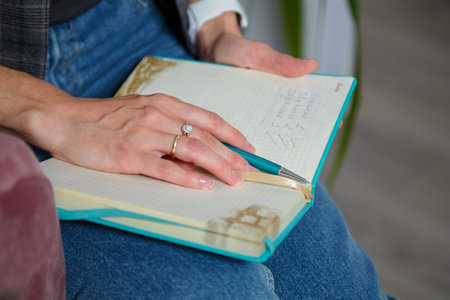 Soft focused close up shot of woman in jeans, gray jacket sitting with notebook, only hands writing...